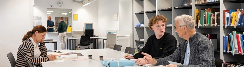 Einige Personen bei der Benutzung von Unterlagen im Lesesaal. Im Hintergrund die Aktenausgabe.